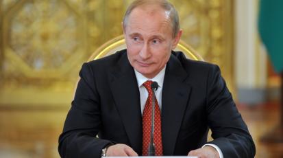 Wladimir Putin sitzt lächelnd auf seinem Platz im Kreml