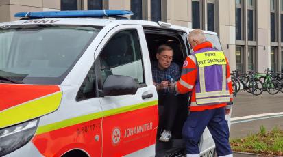 In einem PSNV Einsatzwagen sitzt ein Betroffener der von einer Einsatzkraft betreut wird. Die Einsatzkraft gibt ihm eine Flasche Wasser. Der Wagen gehört zur Johanniter Unfallhilfe und hat ein Blaulicht auf dem Dach.