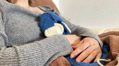 Zu sehen ist ein Ausschnitt, bei dem ein Mädchen eine Wärmflasche gegen ihren Bauch drückt.