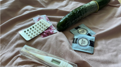 Zu sehen sind die Minipille, ein Basalthermometer, zwei Kondomverpackungen und eine Gurke die mit einem Kondom überzogen ist.