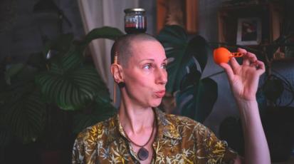 Maria hat ein Glas mit Menstruationsblut auf dem Kopf und hält ihre Menstruationstasse hoch.