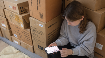 Ein Mädchen sitzt neben gestapelten Kartons und macht online Shopping.