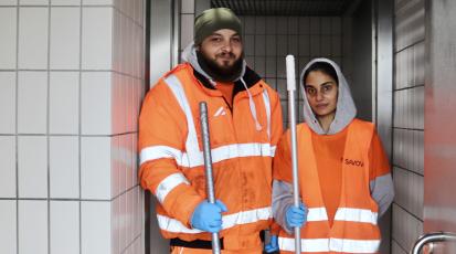 Die beiden Reinigungskräfte stehen nebeneinander im Eingang des Toilettenbereichs.