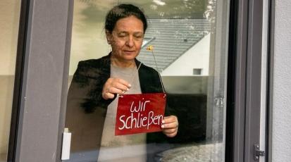 Frau hängt Wir schließen-Schild an Ladentür