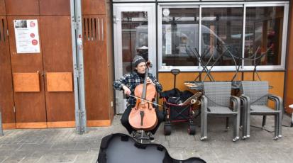 Ein Straßenmusiker ist zu sehen. Vor ihm liegt ein Cellokoffer.