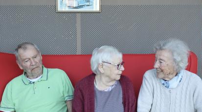 Ein älterer Herr und zwei ältere Damen sitzen nebeneinander auf einem Sofa.