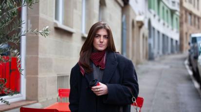 Junge Frau mit rotem Pappbecher in der Hand steht vor einem Café im Stuttgarter Westen.