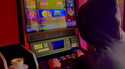 Mann mit schwarzer Kapuze vor Spielautomaten