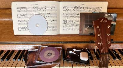 Ein Klavier auf dem verschiedene CDs liegen sowie Kopfhörer und man sieht den Kopf einer Gitarre.