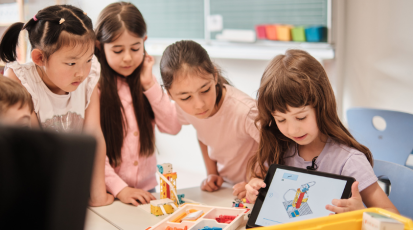 Kids are sitting in a classroom around the table looking at little pieces to build a robot out of lego.