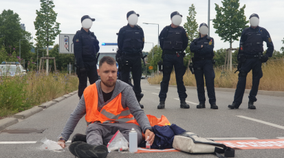Der Klimaaktivist Moritz Riedacher klebt sich auf der Straße fest. Hinter ihm stehen aufgereiht Polizisten.