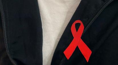 Die Rote AIDS Schleife ist zu sehen, an einem Pulloverkragen.