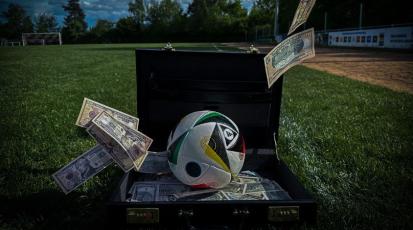 Ein offener Aktenkoffer, gefüllt mit Geldscheinen und einem Fußball, über dem Geld vom Himmel regnet