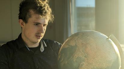 Ein junger Mann schaut auf einen Globus.