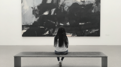 Schwarze Frau sitzt alleine auf einer Bank vor einem Gemälde im Museum