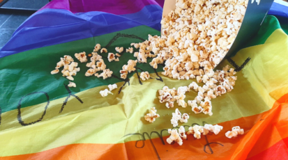 Regenbogenflagge, die auf einem Tisch liegt. Ein Popcorn-Becher liegt auf der Flagge. Popcorn fällt aus dem Popcorn-Becher und liegt auf der Flagge verteilt.