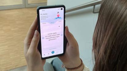 Eine Studentin hält ihr Handy, auf dem eine Seite der App zu sehen ist.