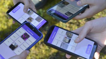 Es wären vier Handpaare zu sehen, die jeweils ein Handy halten. Auf den Displays der Handys ist der Prototyp des "SnapHunt Bingos" zu sehen. Das Bild ist in der Vogelperspektive geschossen.