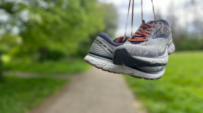 Baumelnde Joggingschuhe vor einer grünen Kulisse.