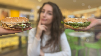 Zwei Hände halten jeweils einen Burger. Dazwischen sitzt eine Frau, die nachdenklich schaut. 