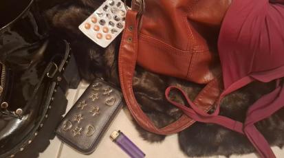 Auf einem Flurboden liegen eine rote Tasche, Tabletten, ein Fellmantel, schwarze Plateauschuhe, ein Geldbeutel und ein Feuerzeug.