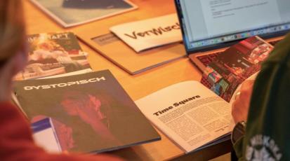 Mehrere Magazine liegen auf einem Tisch verteilt und werden von zwei jungen Frauen betrachtet.