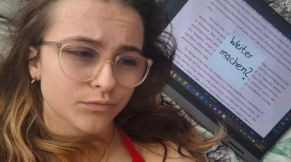Eine Frau liegt mit erschöpftem Blick neben ihrem Laptop. Auf dem Laptop klebt ein Post-it mit der Aufschrift „Weiter machen?“.