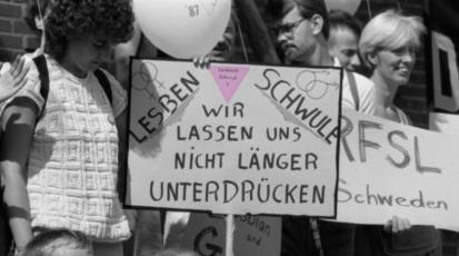 Auf dem Plakat der Demonstrierenden steht neben einem rosa Winkel "Lesben Schwule wir lassen uns nicht mehr unterdrücken".