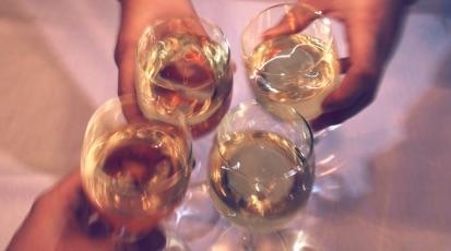 Hände die Gläser mit Weißwein halten und anstoßen.