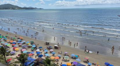Strand mit vielen Sonnenschirmen im Sand. Im Meer sind Menschen die baden.