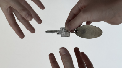 Eine Hand übergibt einen Wohnungsschlüssel mit leerem Anhänger an zwei ausgestreckte Hände … – Symbolbild für den Zugang zu Wohnraum.