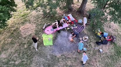 Junge Leute sind aus der Vogelperspektive im Wald zu sehen. Sie liegen auf Picknickdecken und es gibt ein Lagerfeuer.