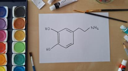 Chemisches Formelzeichen von Dopamin auf Papier gemalt. Daneben ein Wasserfarbkasten und Pinsel.