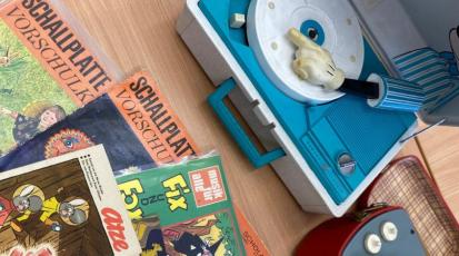 Comics aus den 50ern und 60ern und ein Plattenspieler liegen auf einem Tisch.