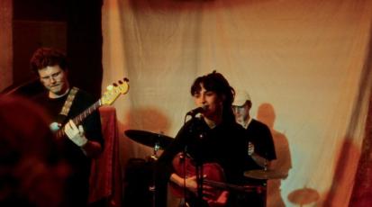 Jasmin sitzt mit einer Violine auf der Bühne und singt. Hinter ihr sitzen zwei ihrer Kommilitonen. Einer am Schlagzeug, der andere an der Gitarre.