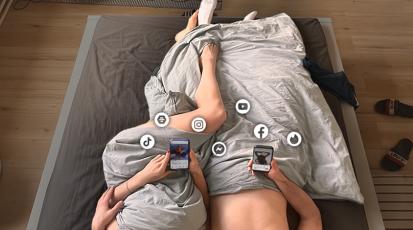 Zwei Menschen im Bett an ihren Smartphones. Zwischen Intimität und Freiheitsdrang