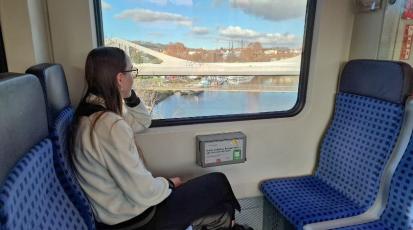 Junge Frau sitzt rechts im Bild in der Bahn und schaut aus dem Fenster.