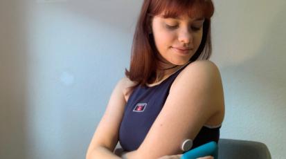 Bild von einer Person die ein Blutzuckermessgerät an den Blutzuckersensor an ihrem Arm hält.