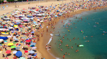Crowded beach in Spain during the summer season with many tourists swimming and sunbathing along the coastline.