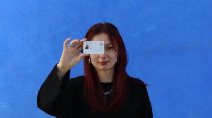 Eine Studentin hält ihren Studentenausweis vor ihrem Gesicht, sodass ein Auge verdeckt ist.