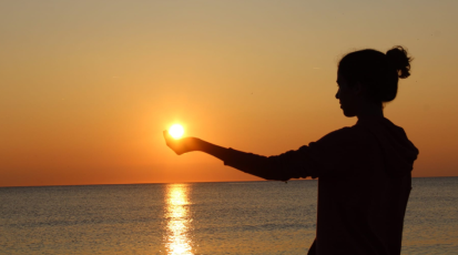 Eine junge Frau hält am Strand ihre Hand der Sonne entgegen. | Bild: Kim Romagnoli