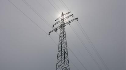 Strommast vor bewölktem Himmel mit leichtem Sonnenschein