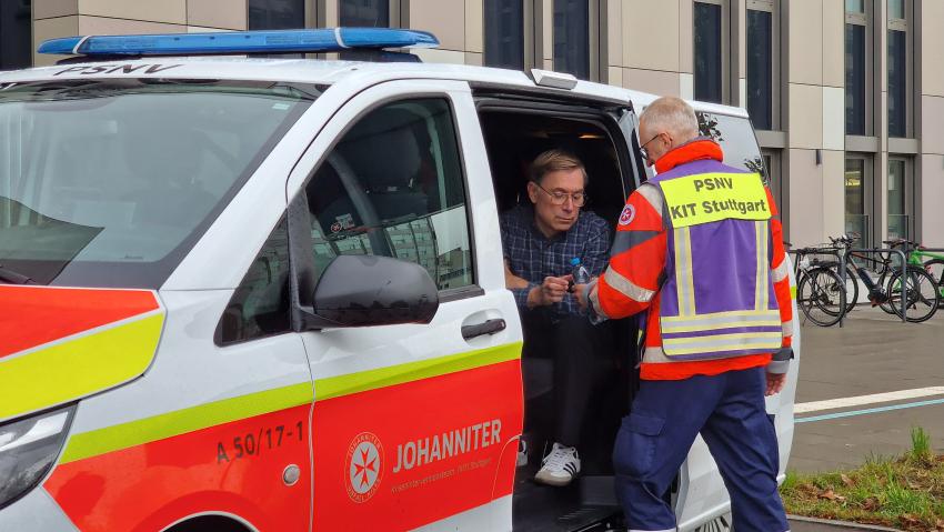 In einem PSNV Einsatzwagen sitzt ein Betroffener der von einer Einsatzkraft betreut wird. Die Einsatzkraft gibt ihm eine Flasche Wasser. Der Wagen gehört zur Johanniter Unfallhilfe und hat ein Blaulicht auf dem Dach.