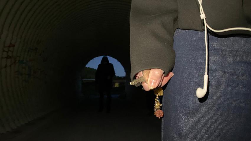 Eine Frau hält einen Schlüssel in der Hand. Hinter ihr ist eine dunkle Gestalt zu sehen.