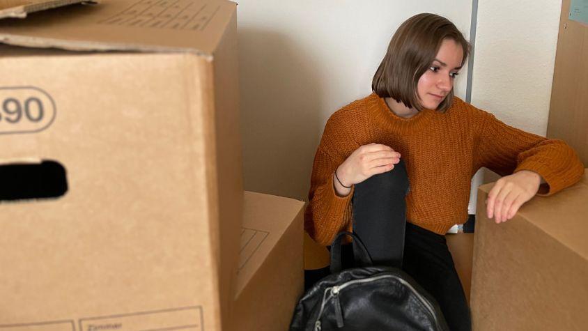 Eine junge Frau sitzt in ihrer Wohnung zwischen Umzugskartons. (Symbolbild) 