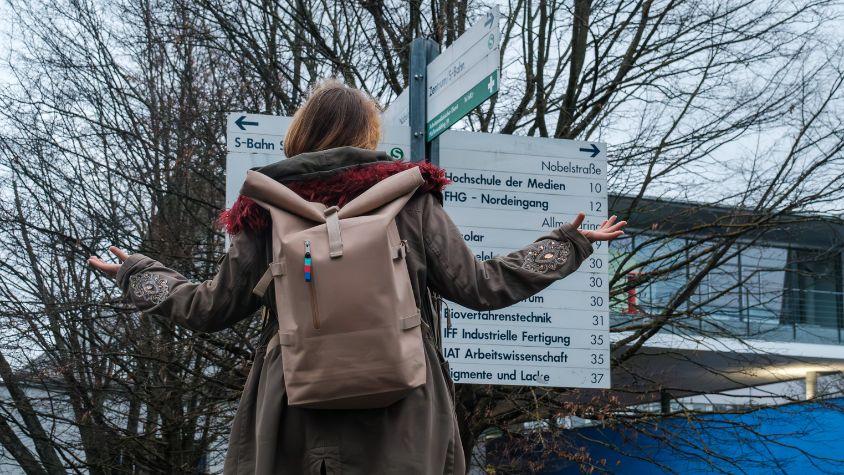 young woman stands questioningly in front of a sign at the university