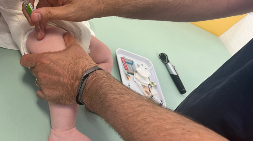 Man sieht den Arm eines Mannes, der ein Baby in den Oberschenkel impft.