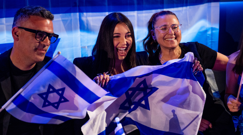 Die Teilnehmerin aus Israel 2025 lächelt mit der Israel Flagge.