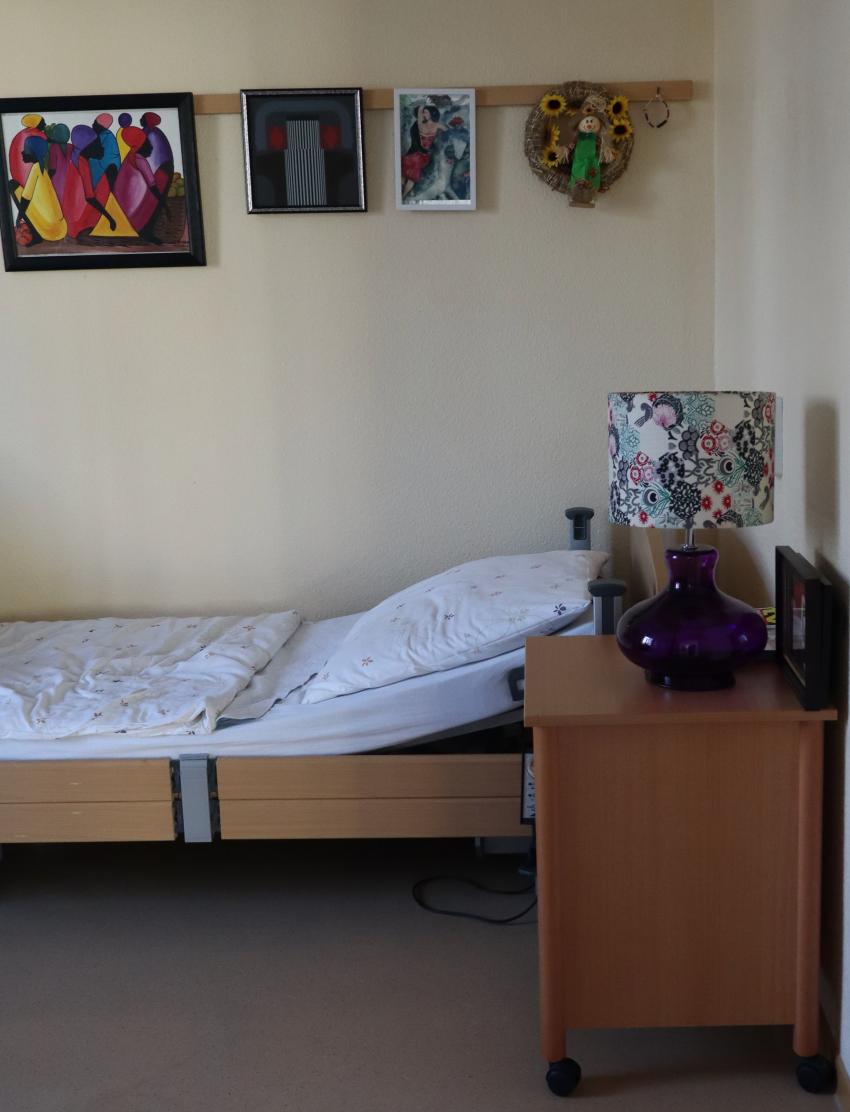 An der Wand hinter einem Bett hängen bunte Bilder.