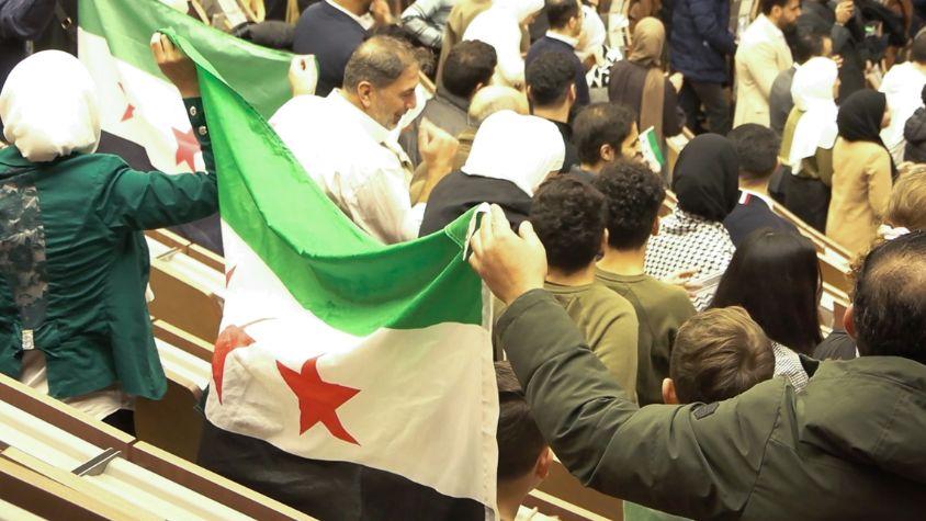 Auf einer deutsch-syrischen Versammlung feiern die Teilnehmenden und halten die Flagge ihres Heimatlandes in die Luft.